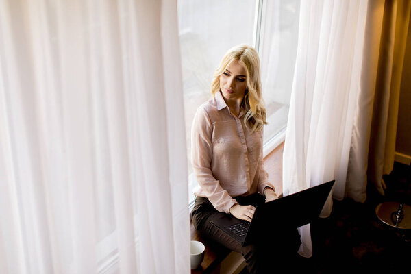 Pretty young woman using laptop and sitting by window