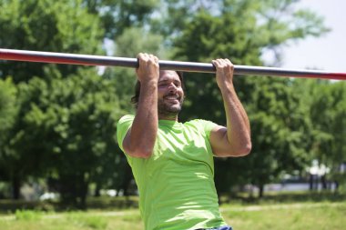 Parkın yatay çubuğunda barfiks çeken kaslı adam.