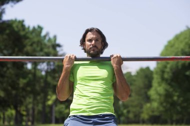 Parkın yatay çubuğunda barfiks çeken kaslı adam.