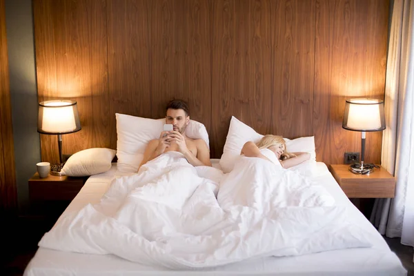 Hombre Joven Mirando Teléfono Mientras Mujer Duerme Habitación — Foto de Stock