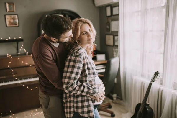 Pregnant woman and happy man in the house standing hugged in the room