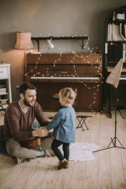 Genç Baba ve küçük kızı evde odada akustik gitar çalmak