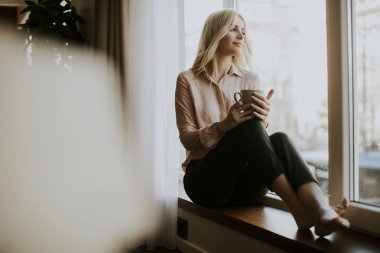 Rahatlatıcı ve içme kahve cam kenarında sarışın genç kadın