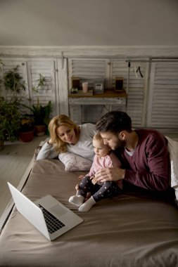Mutlu aile yatak ve yatak odasında dizüstü bilgisayarda bir şey izlerken yatıyor