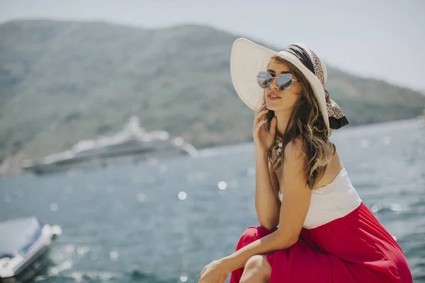 漂亮的年轻女子戴着帽子和太阳镜坐在海边 — 图库照片
