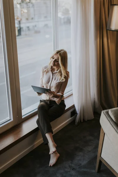 Young businesswoman with tablet sitting by window in the room