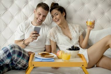 Yatakta kahvaltı ve cep telefonu arayan genç Çift