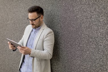 Gri duvar tarafından dijital tablet ile yakışıklı genç işadamı