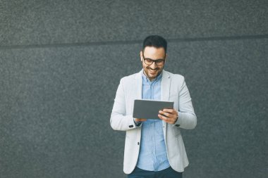 Gri duvar tarafından dijital tablet ile yakışıklı genç işadamı