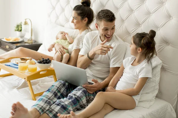 Young family with laptop in the bed