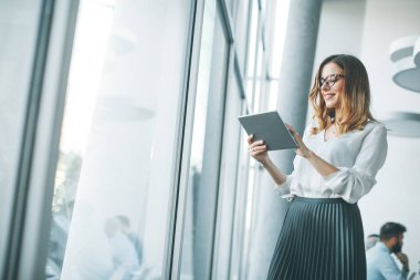 Genç çekici kadın Yöneticisi duran modern Office dijital tablet üzerinde çalışan