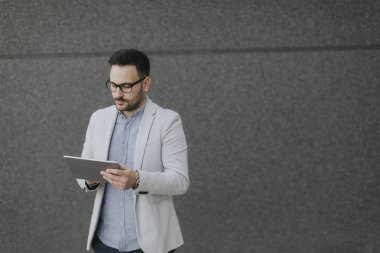 Gri duvar tarafından dijital tablet ile yakışıklı genç işadamı