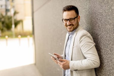Gri duvar tarafından dijital tablet ile yakışıklı genç işadamı