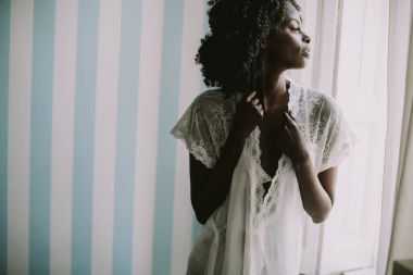 Afrikalı-Amerikalı kadın pencerenin yanındaki odada poz