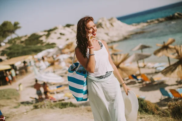 年轻漂亮的女人 与在夏天谈移动电话在海边的沙滩袋 — 图库照片