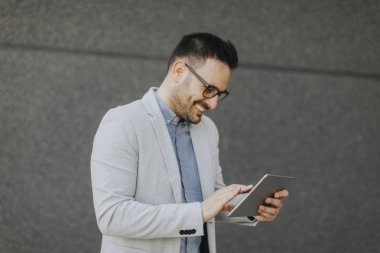 Gri duvar tarafından dijital tablet ile yakışıklı genç işadamı