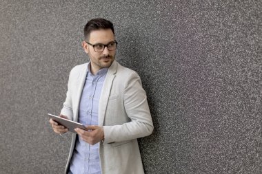 Gri duvar tarafından dijital tablet ile yakışıklı genç işadamı