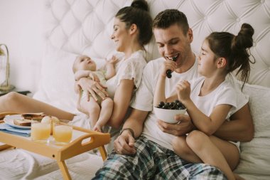 Anne, baba, Bebek ve küçük kız yatakta üzüm yemek