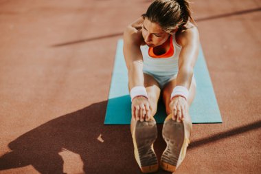 Sportif genç bayan dışarıda esneme hareketleri yapıyor.