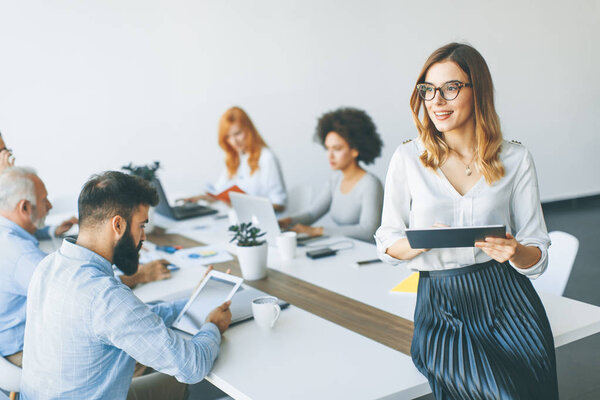 Молодая привлекательная женщина-менеджер работает на цифровой планшет, стоя в современном офисе
