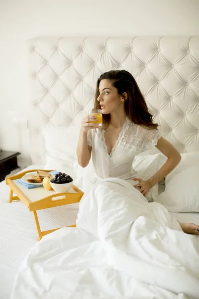 漂亮的年轻女子在卧室的床上吃早餐和喝新鲜橙汁 — 图库照片