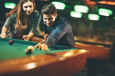 Genç çift barda bilardo oynuyor.