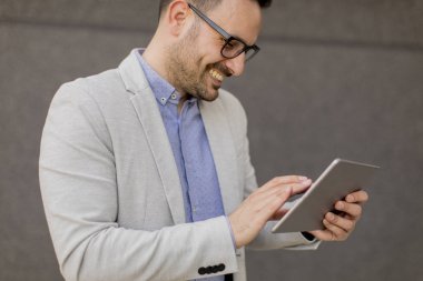 Gri duvar tarafından dijital tablet ile yakışıklı genç işadamı