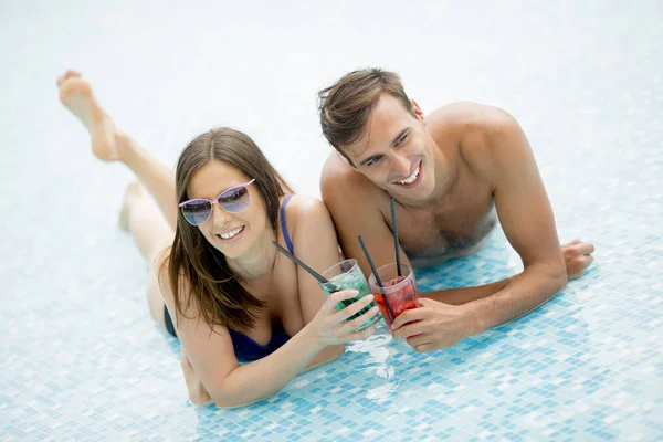 年轻夫妇在夏季的游泳池里喝鸡尾酒 — 图库照片