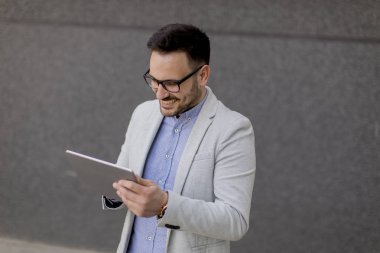 Gri duvar tarafından dijital tablet ile yakışıklı genç işadamı