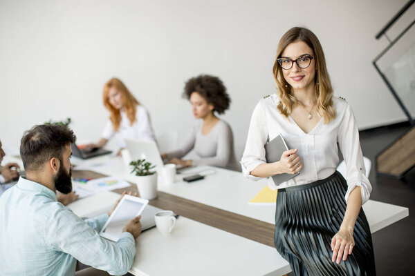 Молодая привлекательная женщина-менеджер работает на цифровой планшет, стоя в современном офисе
