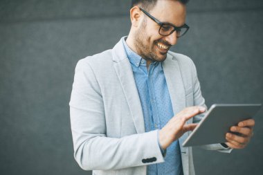 Gri duvar tarafından dijital tablet ile yakışıklı genç işadamı