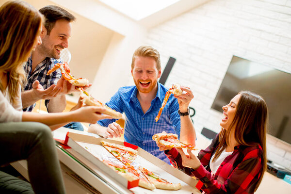 Group of young friends eating pizza at home and having fun