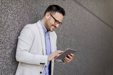 Gri duvar tarafından dijital tablet ile yakışıklı genç işadamı