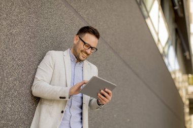 Gri duvar tarafından dijital tablet ile yakışıklı genç işadamı