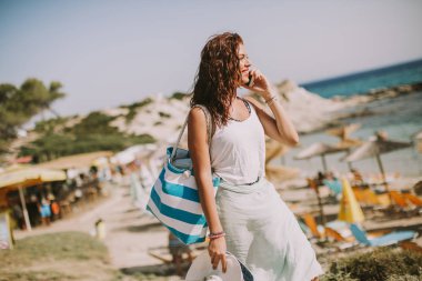 Cep telefonuyla sahilde güneşli yaz gününde bir çanta ile genç ve güzel kadın
