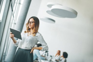 Genç çekici kadın Yöneticisi duran modern Office dijital tablet üzerinde çalışan