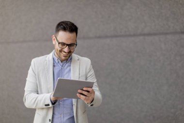 Gri duvar tarafından dijital tablet ile yakışıklı genç işadamı