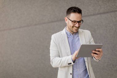 Gri duvar tarafından dijital tablet ile yakışıklı genç işadamı