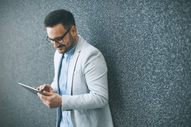 Gri duvar tarafından dijital tablet ile yakışıklı genç işadamı