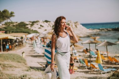 Cep telefonuyla sahilde güneşli yaz gününde bir çanta ile genç ve güzel kadın