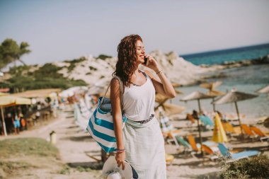 Cep telefonuyla sahilde güneşli yaz gününde bir çanta ile genç ve güzel kadın