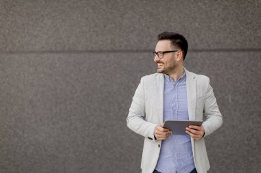 Gri duvar tarafından dijital tablet ile yakışıklı genç işadamı