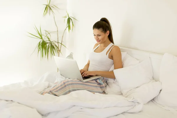 面带笑容的女人赶上她的社交媒体 如她放松躺在床上有一台笔记本电脑上慵懒的一天 — 图库照片