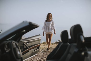 Yazın deniz kenarındaki beyaz atlı aracın yanında güzel bir genç kadın.