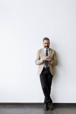 Ofisteki duvara karşı cep telefonu kullanan yaşlı sakallı bir işadamı.