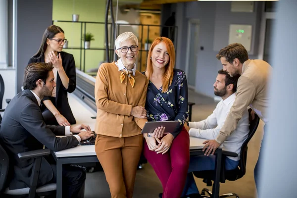 Happy business women working together online on a digital tablet in front of young team at the office