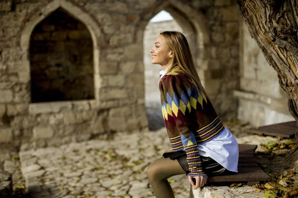 Pretty young woman sitting on the bench watching yellow leaves tree in the autumn park