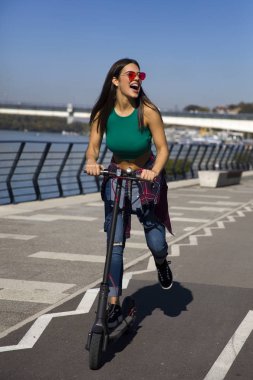 Güneşli bir günde sokakta elektrikli scooter süren güzel bir genç kadın.
