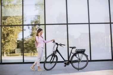 Young woman with ebicycle using on mobile phone outdoor