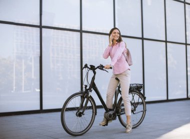 Young woman with ebicycle using on mobile phone outdoor